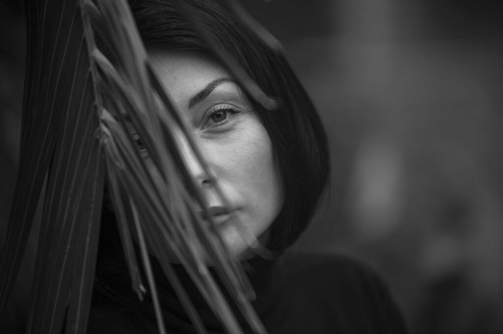 Artistic black and white portrait of a woman partially obscured by leaves, creating a mysterious look.